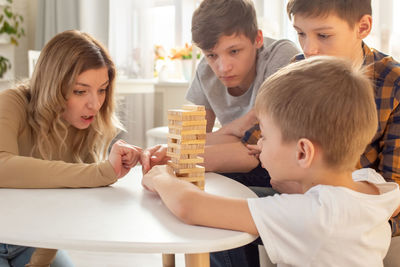 A mother and three sons are enthusiastically playing a board game made of wooden rectangular blocks