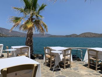 Chairs and table by sea against clear sky