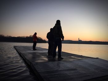 Men standing on floating platform at lake during sunset