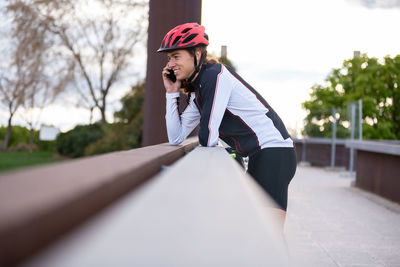 Side view of smiling man listening over phone while standing on bridge