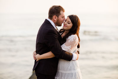 Newlyweds standing on rock at beach in san diego during sunset