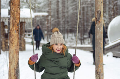 Woman sitting on swing on snow covered field during winter