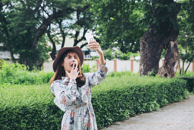 Surprised young woman using mobile phone while standing at public park