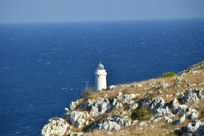 Lighthouse by sea and buildings against sky