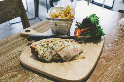 High angle view of chicken parma served with french fries on cutting board at table