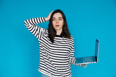 Portrait of young woman standing against blue background