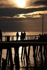 Silhouette people on pier against sea during sunset