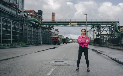 Full length portrait of woman standing with arms crossed on road in city