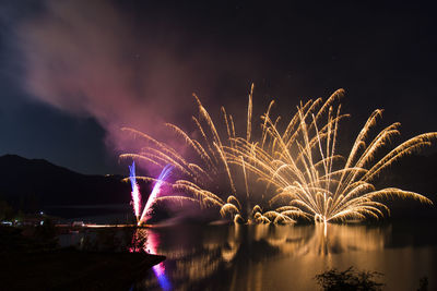 Firework display over river against sky at night