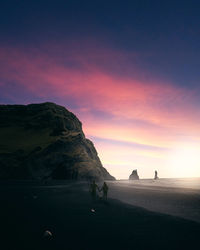 People on beach against sky during sunset