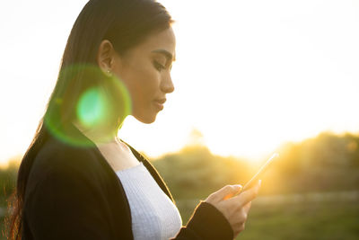 Portrait of young woman using smart phone against sky