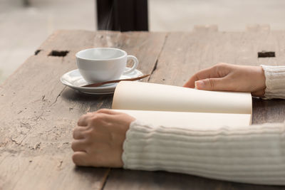 Close-up of hand holding coffee cup on table