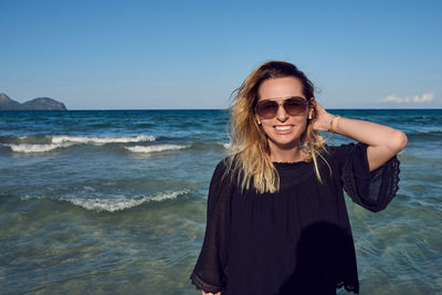 Portrait of smiling mature woman standing at beach against clear sky