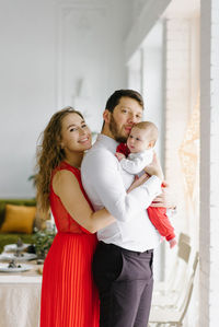 Portrait of a beautiful family with their son in their arms standing near the window 