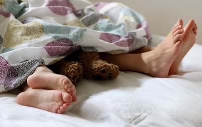 Low section of children sleeping with teddy bear on bed at home