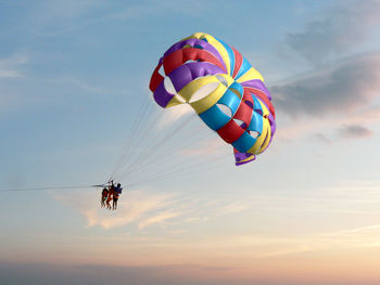 Low angle view of people parasailing against sky during sunset