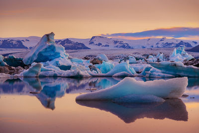 Frozen lake against mountain during sunset