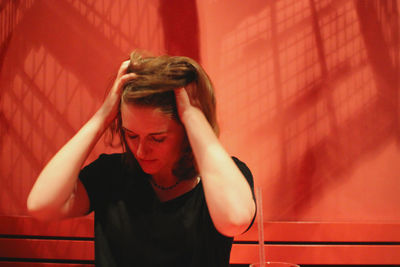 Beautiful blond woman suffering from headache against red wall