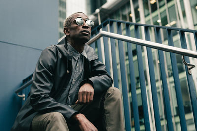 Low angle view of man looking away while sitting on railing