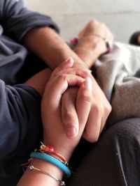 Midsection of couple holding hands while sitting at home