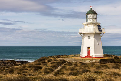 Nugget point lighthouse by sea against cloudy sky