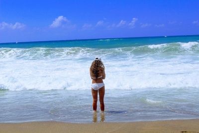 Rear view of woman standing on beach against sky