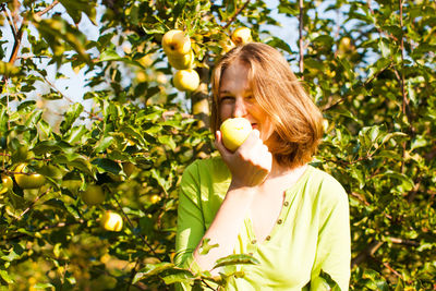 Portrait of woman holding apple against tree
