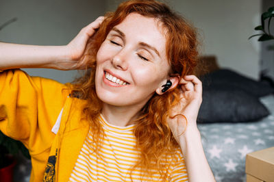 Happy red-haired girl listening music, at home in wireless headphones