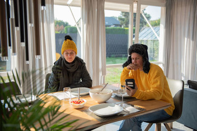 A couple is sitting at the dining table in winter clothes at home, it is cold, they are freezing