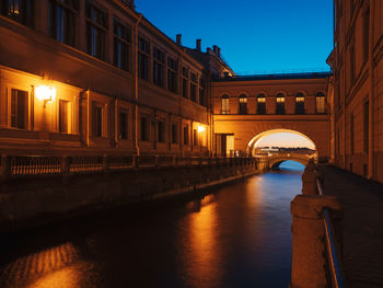 Illuminated bridge over canal amidst buildings at night