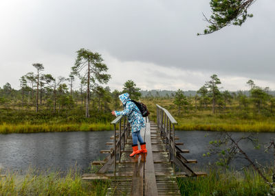 Rear view of woman walking on boardwalk against sky, swamp landscape