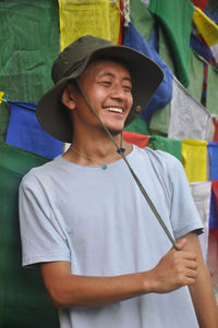 A happy tibetan young man looking sideways, standing against buddhist prayer flags 