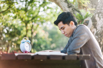 Young man reading book at table in park