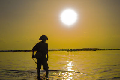 Rear view of silhouette man standing in sea against sky during sunset