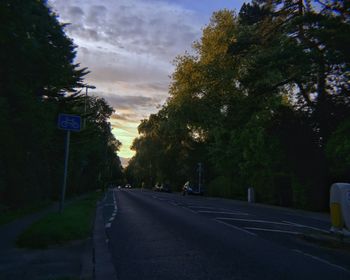 Road sign by trees against sky