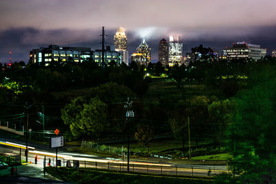 Illuminated street amidst buildings against sky at night