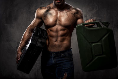 Midsection of muscular worker holding cans while standing against wall