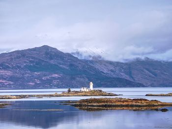 Isle ornsay lighthouse built on a small isle located on ferry route. low water. snowy mountain