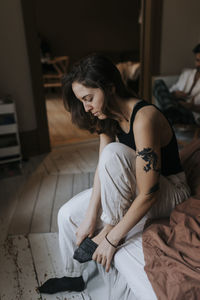 Non-binary person wearing sock while sitting on bed at home