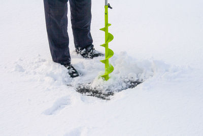 Low section of person drilling frozen lake by snow during winter
