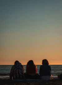 People sitting by sea against sky during sunset