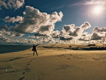 Man standing at beach against cloudy sky