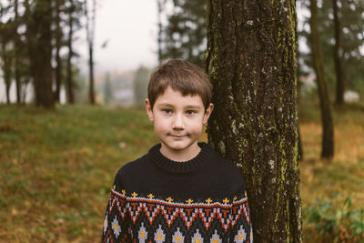 Portrait of cute boy standing by tree at forest