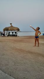 Optical illusion of boy holding sun while standing on sand at beach during sunset