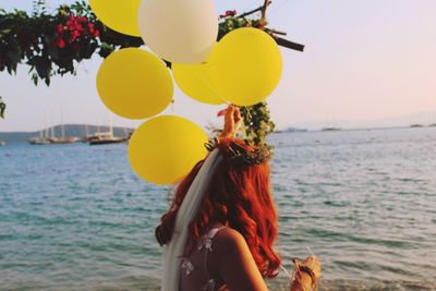 Side view of bride holding balloons while standing at beach