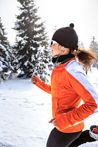 Woman running on snow covered field against sky