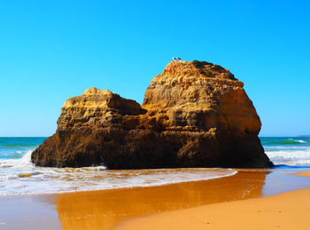 Rock formation on beach against clear blue sky