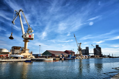 Cranes at harbor against sky