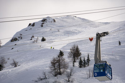 Overhead cable car on snow covered mountains against sky