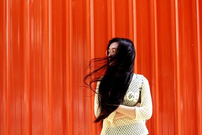 Woman with tousled hair standing against orange wall